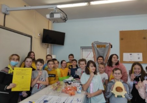Zdjęcie przedstawia uczniów kl. 5 b wraz z nauczycielką geografii p. Aleksandrą Zagner, która trzyma w dłoni tekst przyrzeczenia Klasowych Ambasadorów Życzliwości.